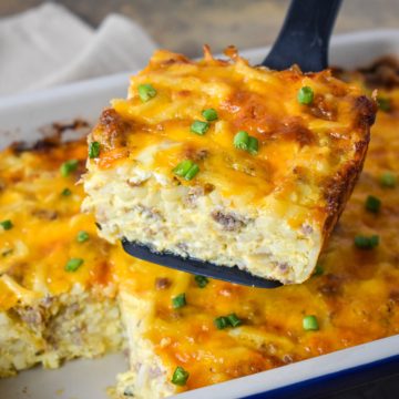 A portion of the sausage hash brown casserole held up over the baking dish by a black spatula.