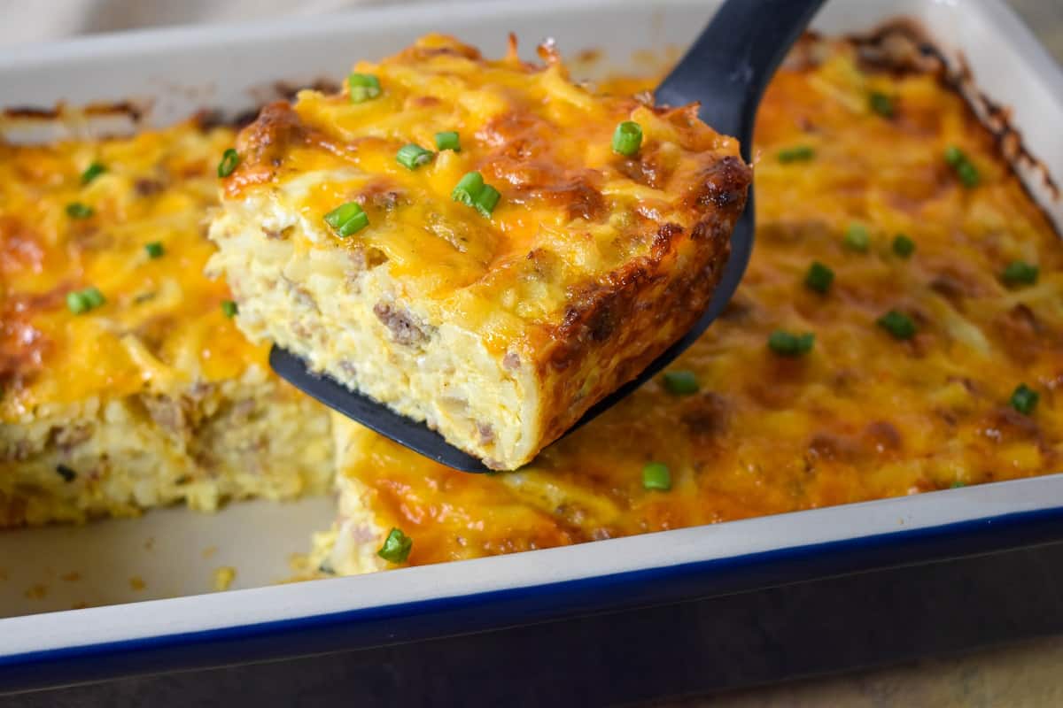 A portion of the sausage hash brown casserole held up over the baking dish with a black spatula.