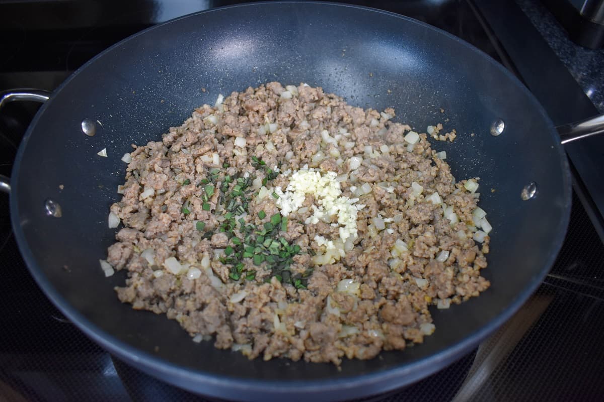 Garlic and minced sage added to the browned sausage onion mixture in a large, black pan.