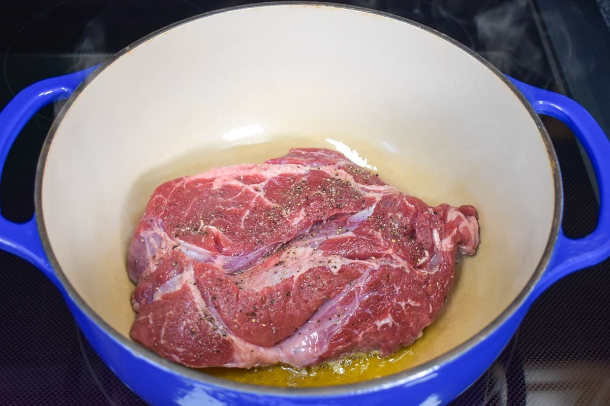 A chuck roast, before browning the top side, in a large, blue dutch oven.