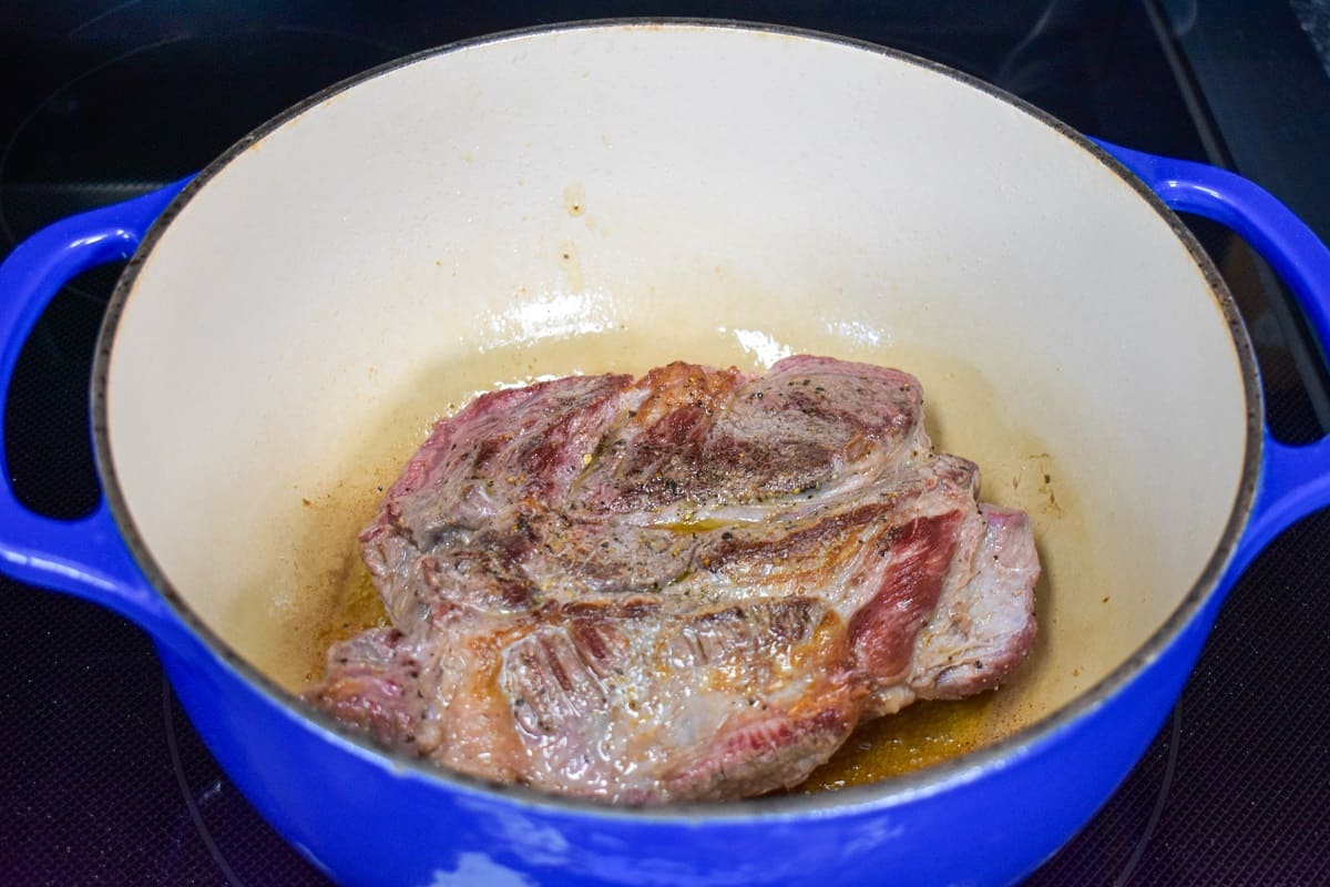A chuck roast, browned side up in a large, blue dutch oven.