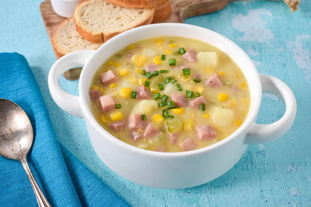 The finished chowder served in a white bowl set on a blue table with sliced bread in the background.