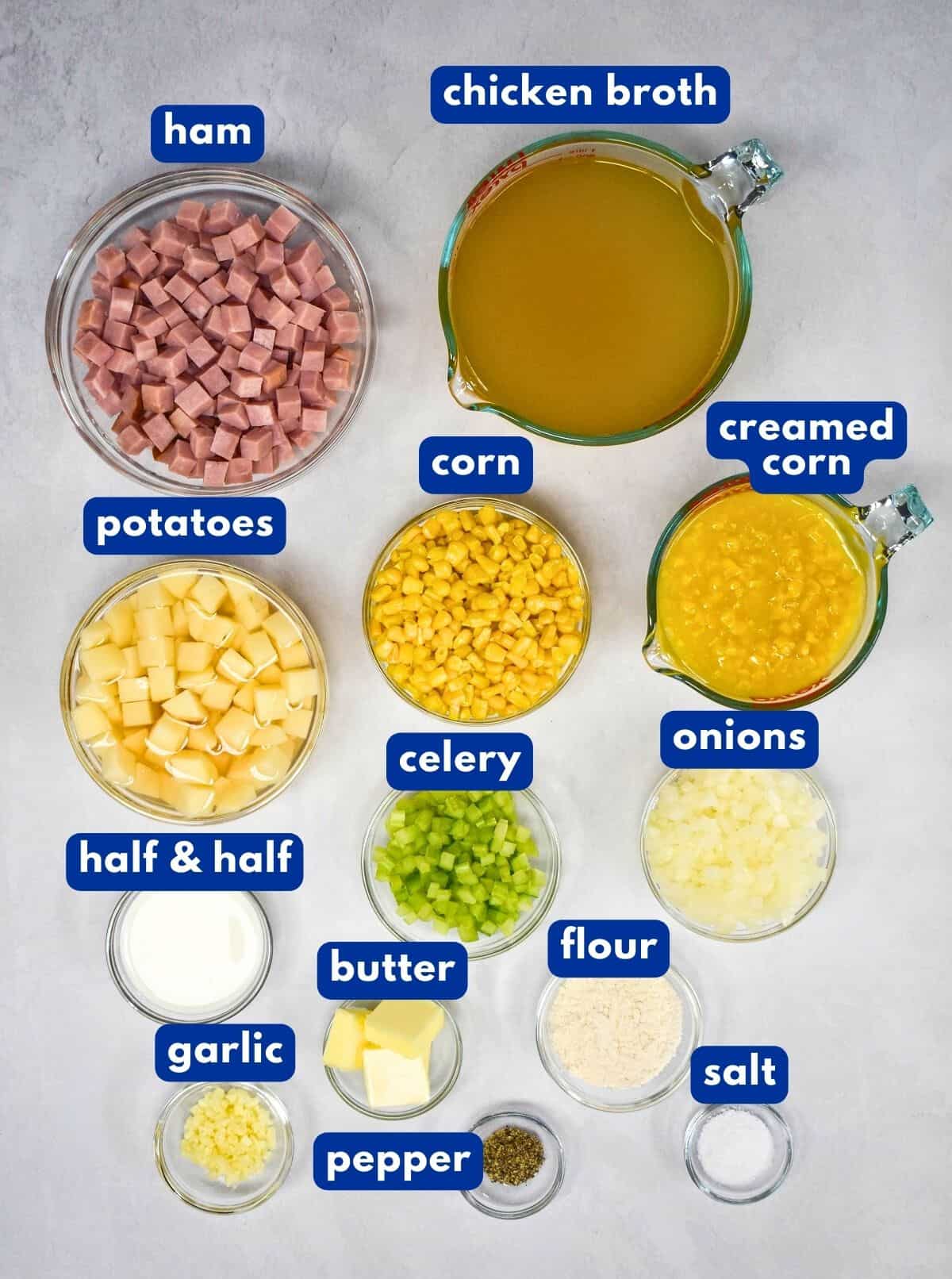 The ingredients for the chowder prepped and arranged in glass bowls on a white table with each labeled with a blue and white tag.