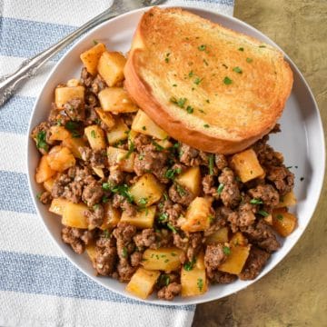 The ground beef and potatoes served on a white plate with a piece of Texas toast.