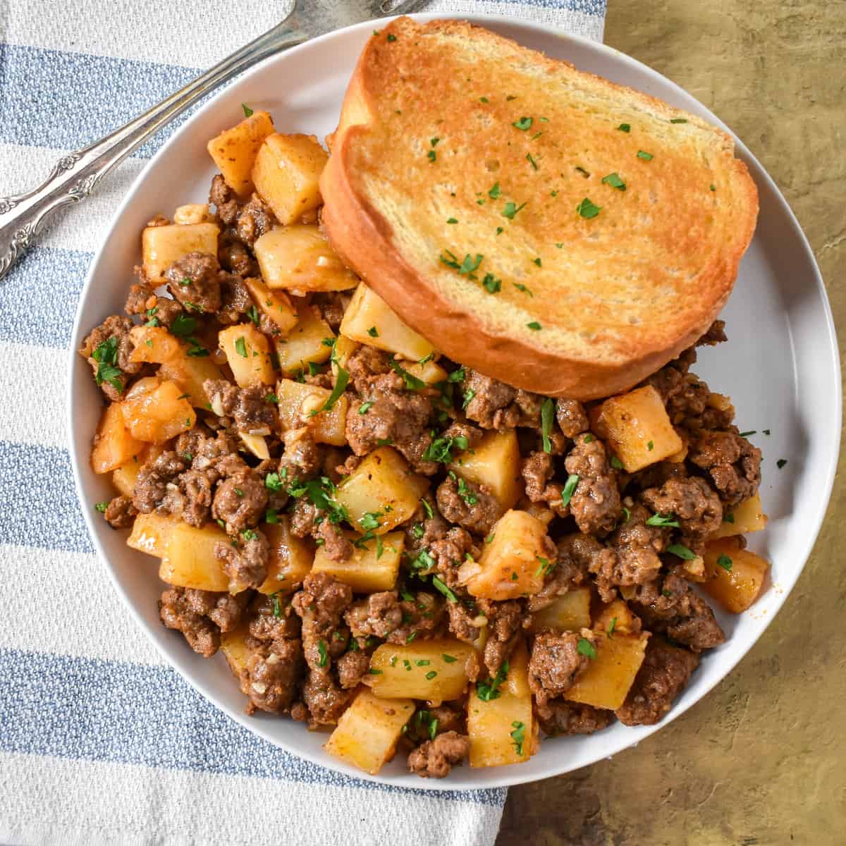 The ground beef and potatoes served on a white plate with a piece of Texas toast.