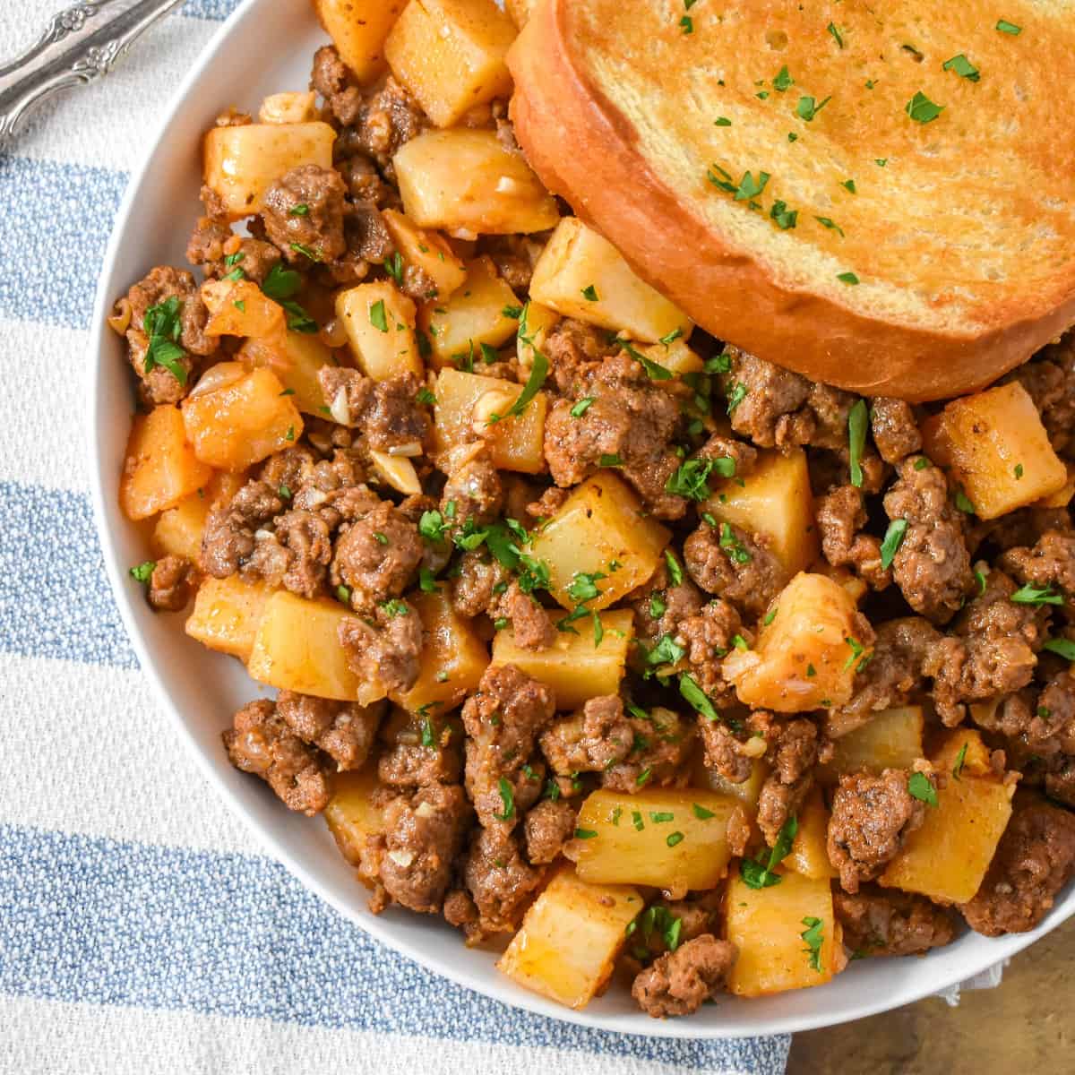 The ground beef and potatoes served on a white plate with a piece of Texas toast.