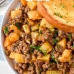 The ground beef and potatoes served on a white plate with a piece of Texas toast.