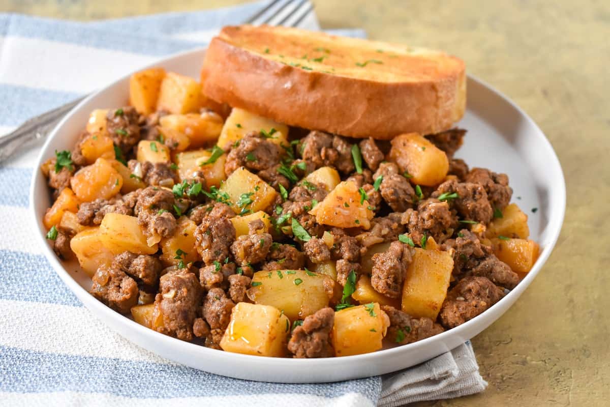 The ground beef and potatoes served on a white plate with a piece of Texas toast.