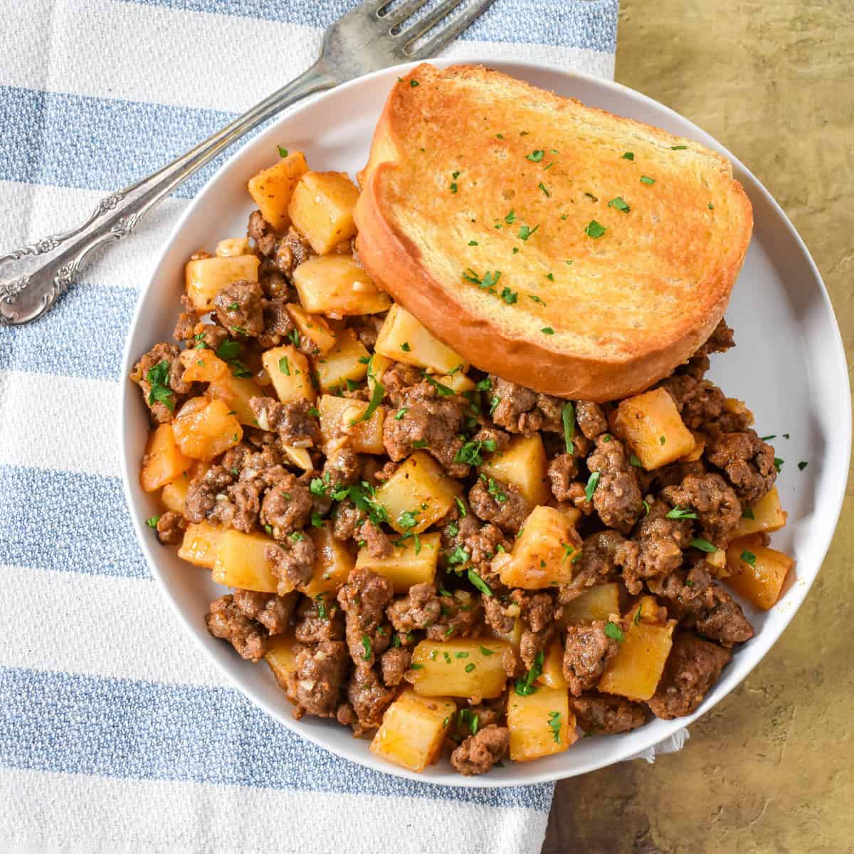 The ground beef and potatoes served on a white plate with a piece of Texas toast.