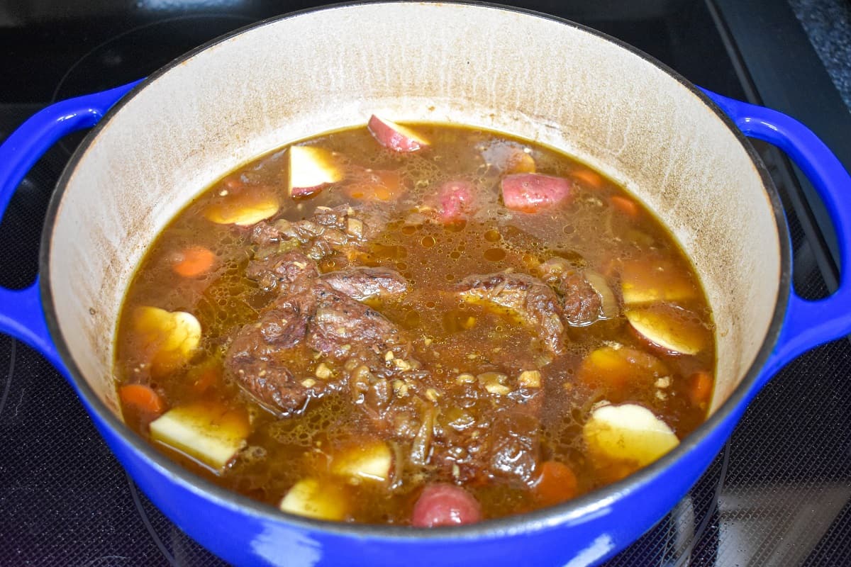Potatoes added to the beef and broth in a large, blue pot.