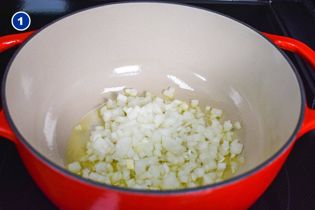 Diced onions cooking in olive oil in a red and white pot.