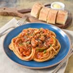 Spaghetti served with the sauce with squash and garnished with chopped parsley and parmesan cheese. Bread slices are in the background on a cutting board with butter.