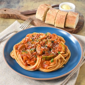 Spaghetti served with the sauce with squash and garnished with chopped parsley and parmesan cheese. Bread slices are in the background on a cutting board with butter.