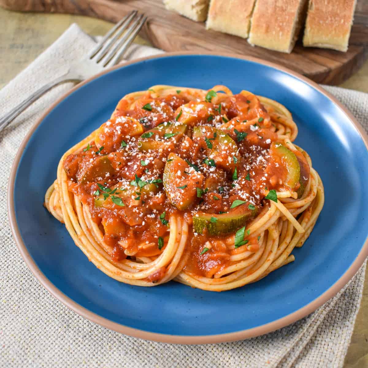 The spaghetti sauce with squash served on a blue plate and garnished with chopped parsley and parmesan cheese.