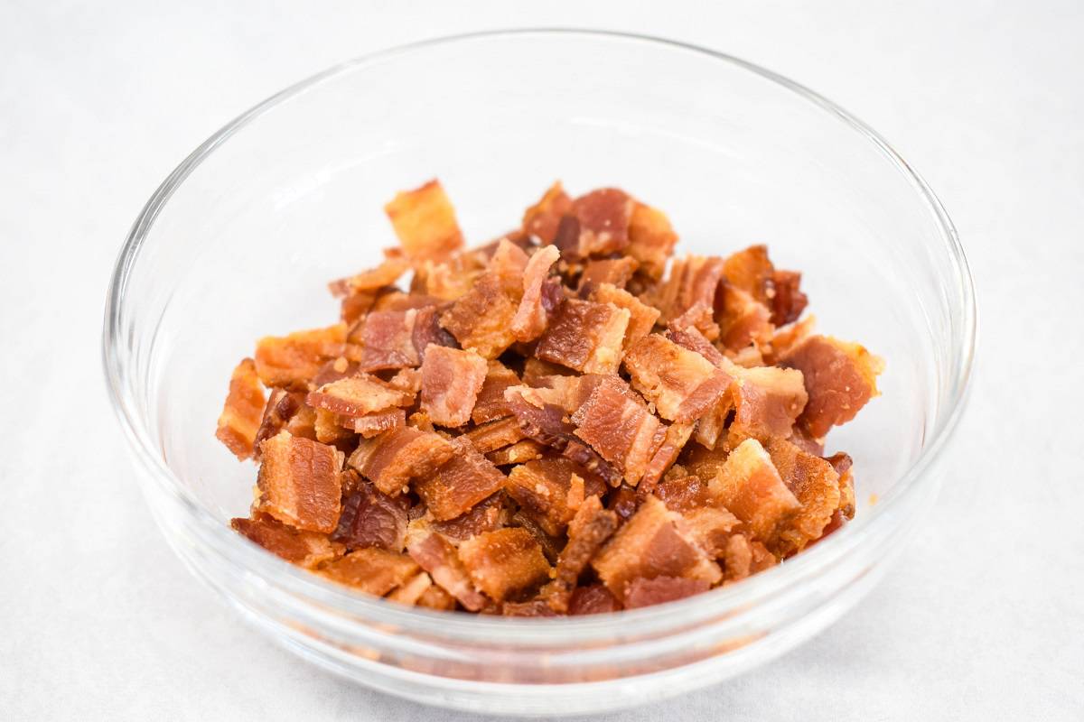 Crispy bacon bits in a glass bowl set on a white table.