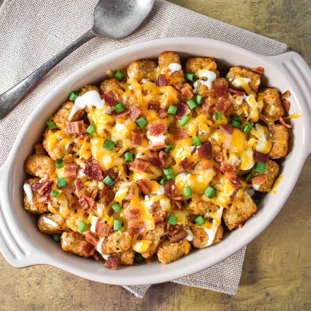 The loaded tater tots in a casserole dish set on a beige linen.