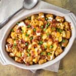 The loaded tater tots in a casserole dish set on a beige linen.