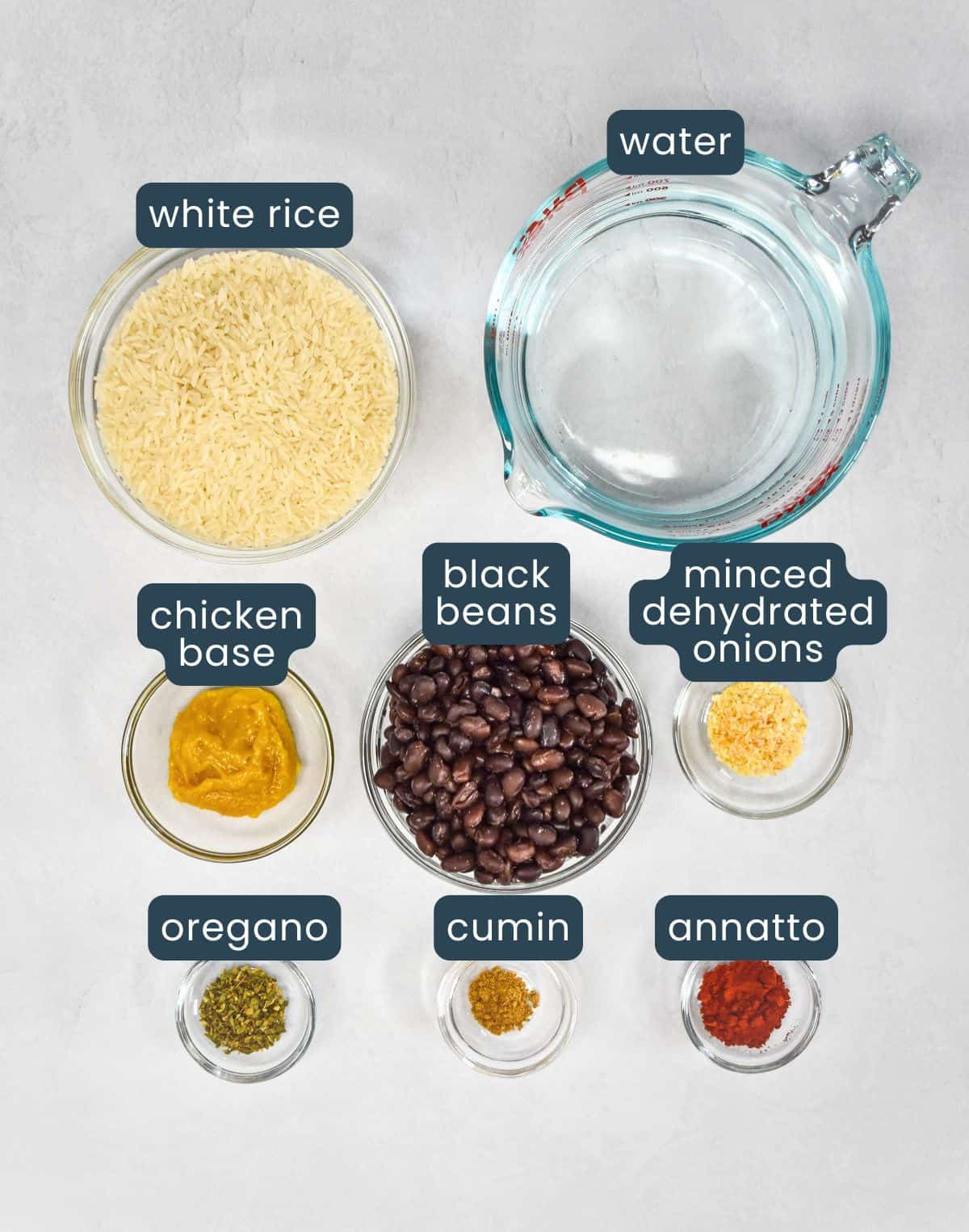 The ingredients for the black beans and yellow rice arranged in glass bowls on a white table with each one labeled.