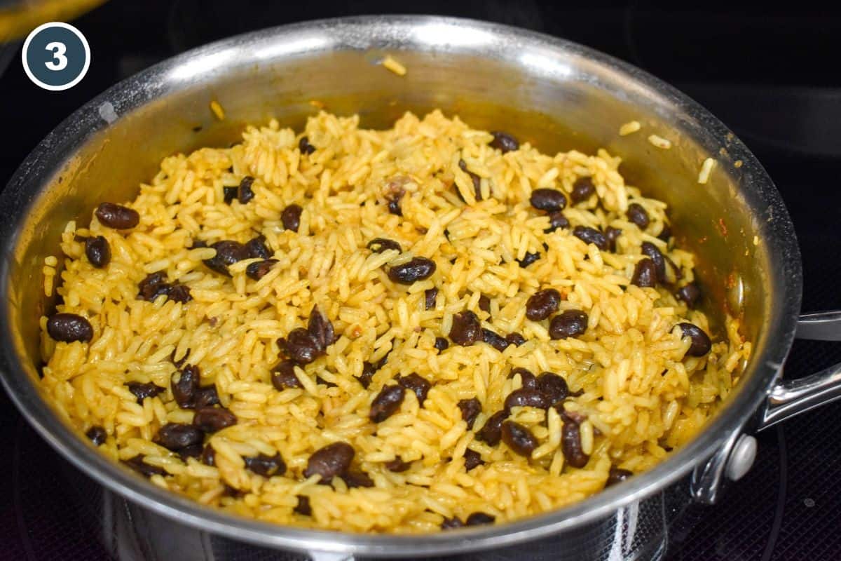 Cooked black beans and yellow rice fluffed together in a saucepan.