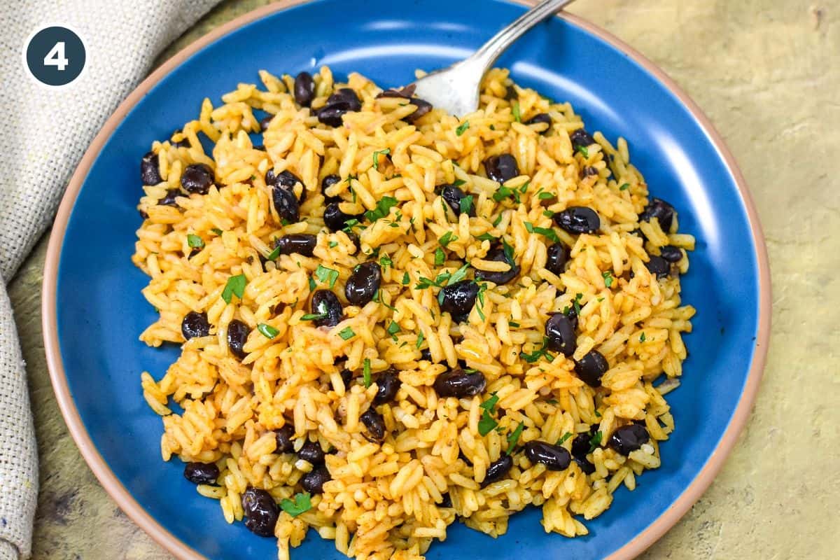 Black beans and yellow rice served in a blue plate and garnished with chopped parsley.