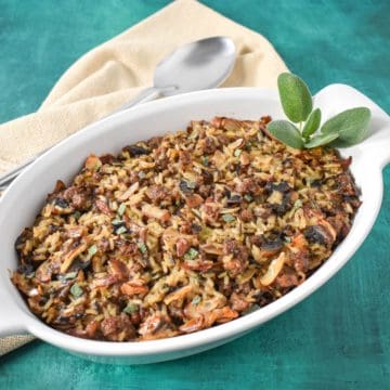 The finished sausage wild rice casserole garnished with sage and set on a green table with a beige linen.