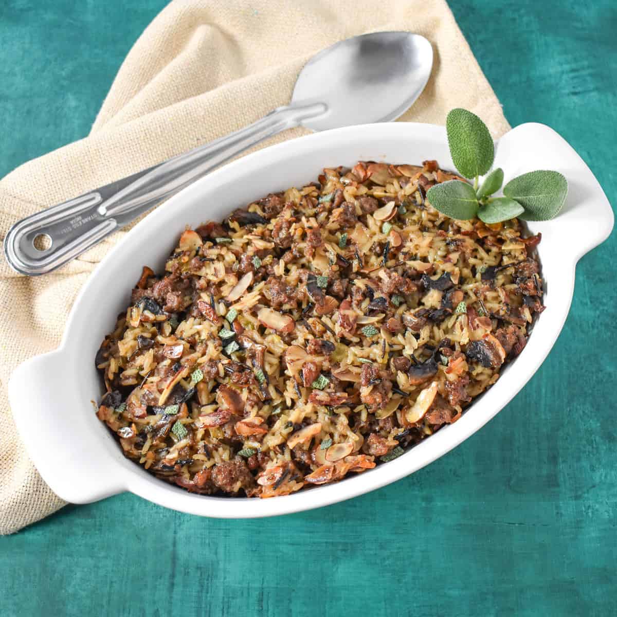 The finished sausage wild rice casserole garnished with sage and set on a green table with a beige linen.