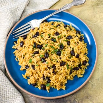 The yellow rice and black beans garnished with chopped parsley and served on a blue plate.