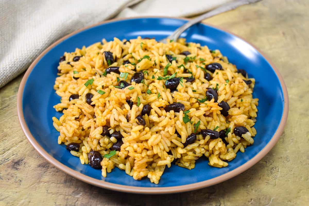 The yellow rice and black beans garnished with chopped parsley and served on a blue plate.