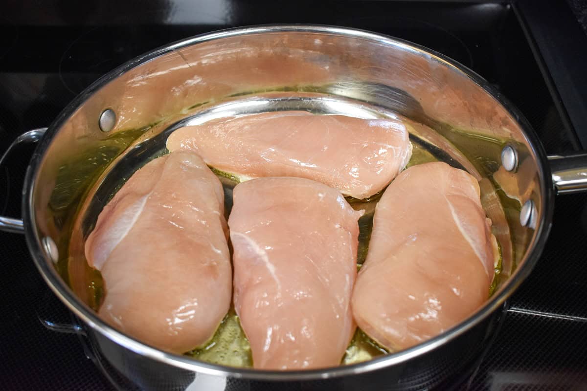 Four large chicken breast arranged in a large saute pan.
