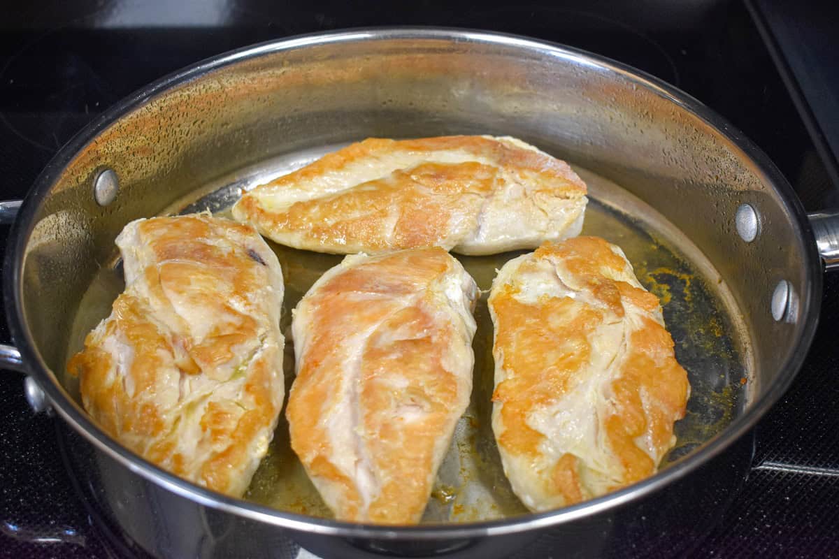 Four large chicken breast arranged in a large saute pan and browned until golden.