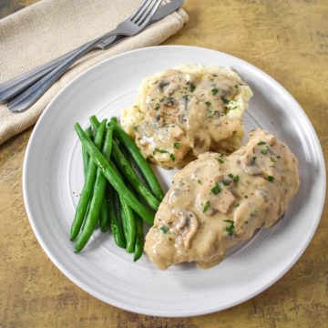 The chicken with the mushroom gravy served on a white plate with mashed potatoes and green beans.