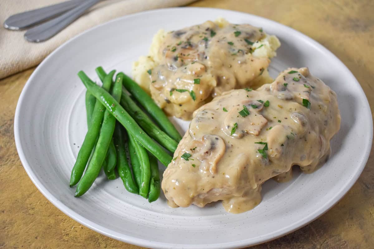 The chicken with the mushroom gravy served on a white plate with mashed potatoes and green beans.