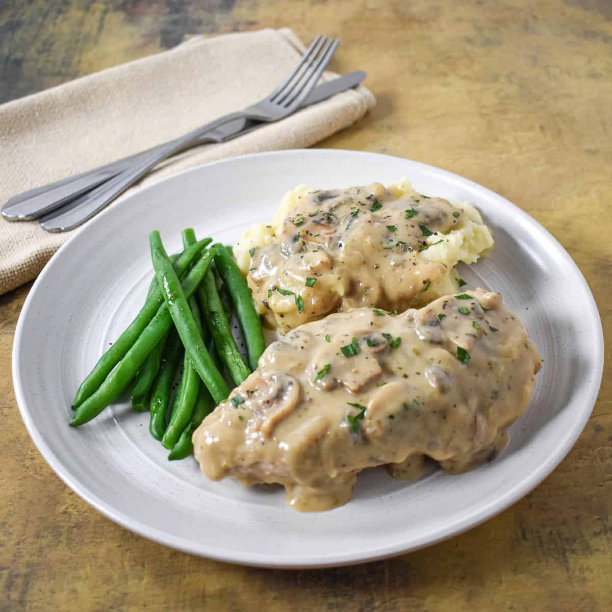 The chicken with the mushroom gravy served on a white plate with mashed potatoes and green beans.