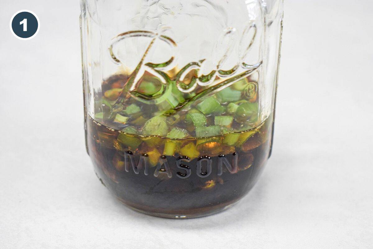 Sesame chicken sauce ingredients, including soy sauce and sliced green onions, combined in a glass mason jar.