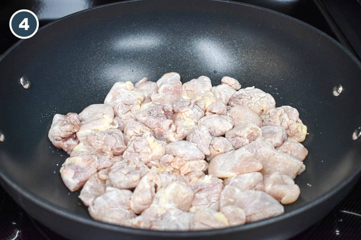 Cornstarch-coated chicken thigh pieces arranged in a large nonstick skillet for cooking.