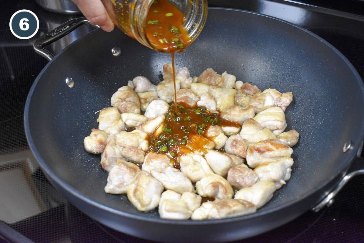 Homemade sesame chicken sauce being poured over browned chicken thigh pieces in a large skillet.