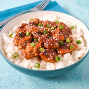 Sesame chicken with chicken thighs served over a bed of white rice in a light blue and white bowl.