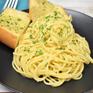 Spaghetti Aglio e Olio served on a black plate with two pieces of garlic toast in the background.