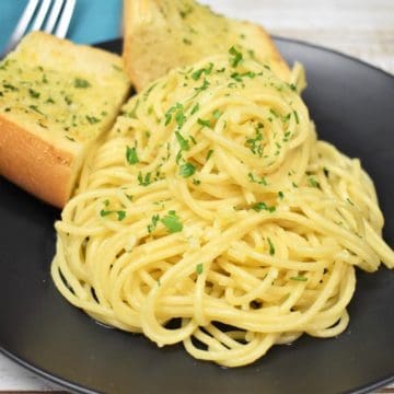 Spaghetti Aglio e Olio served on a black plate with two pieces of garlic toast in the background.