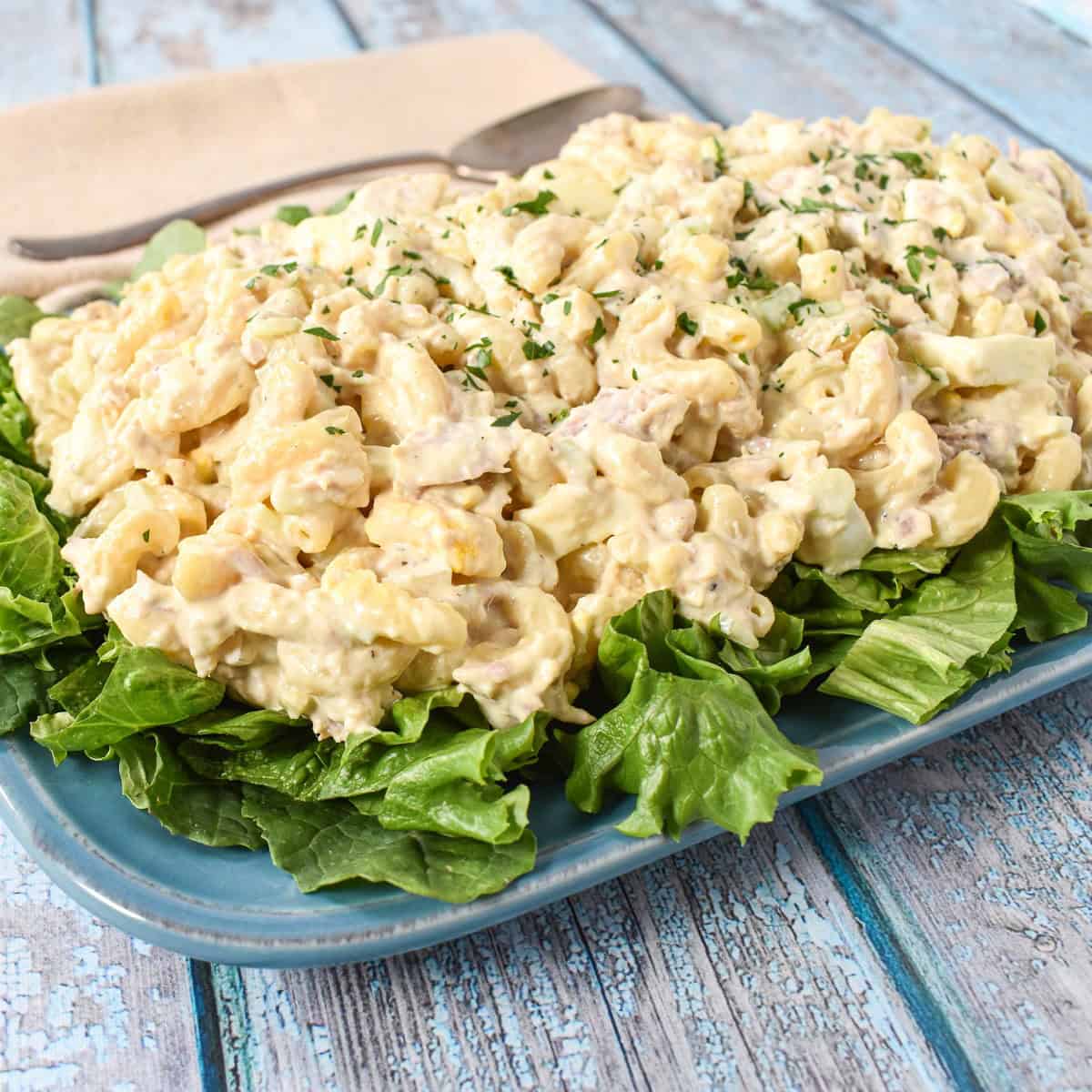 Macaroni tuna salad served on a bed of lettuce on a blue platter.