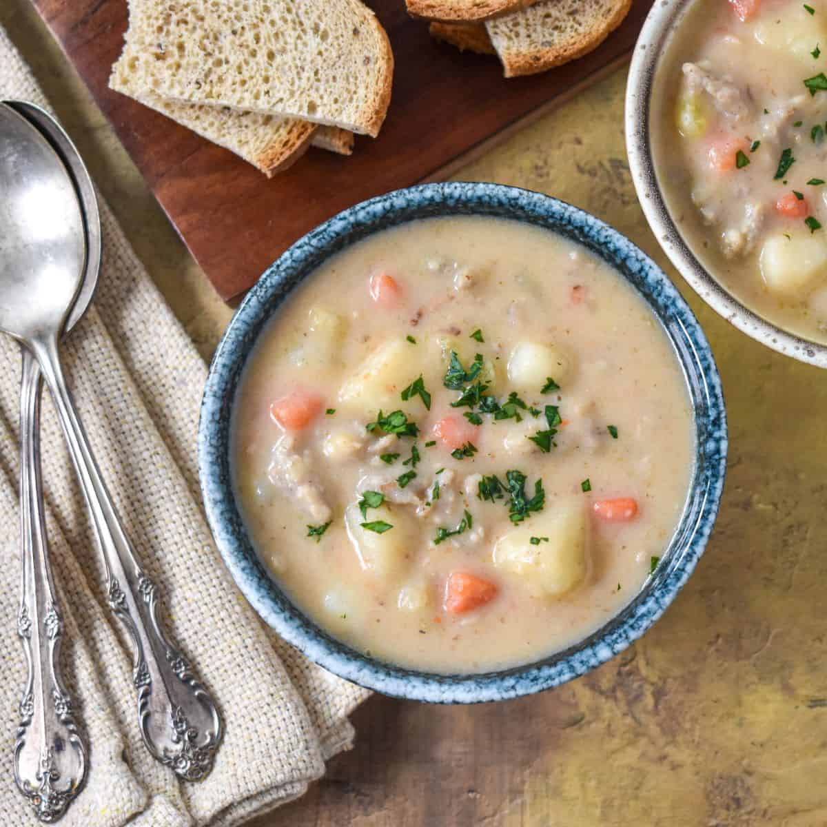 The bratwurst soup served in a blue bowl with sliced bread in the background.