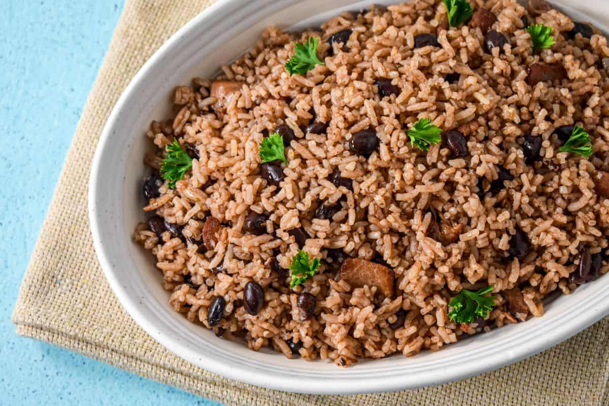 A white serving bowl filled with moros—Cuban black beans and rice—garnished with parsley. The bowl is placed on a beige linen.