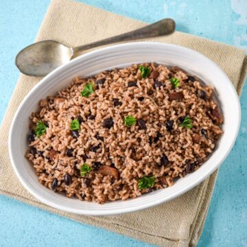 A full view of a white bowl filled with Cuban black beans and rice, topped with fresh parsley and set on a beige linen over a light blue surface.