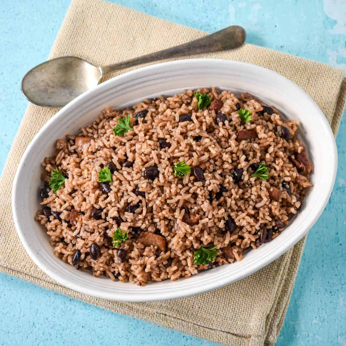 A full view of a white bowl filled with Cuban black beans and rice, topped with fresh parsley and set on a beige linen over a light blue surface.