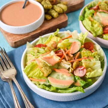 A fresh green salad topped with homemade creamy French dressing, served with a bowl of extra dressing and croutons on the side.
