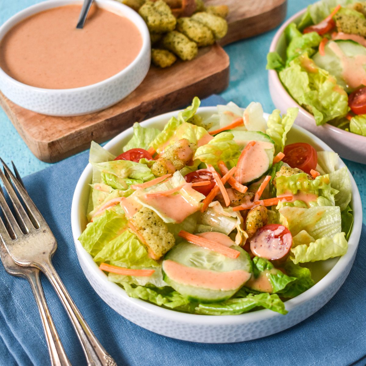 A fresh green salad topped with homemade creamy French dressing, served with a bowl of extra dressing and croutons on the side.