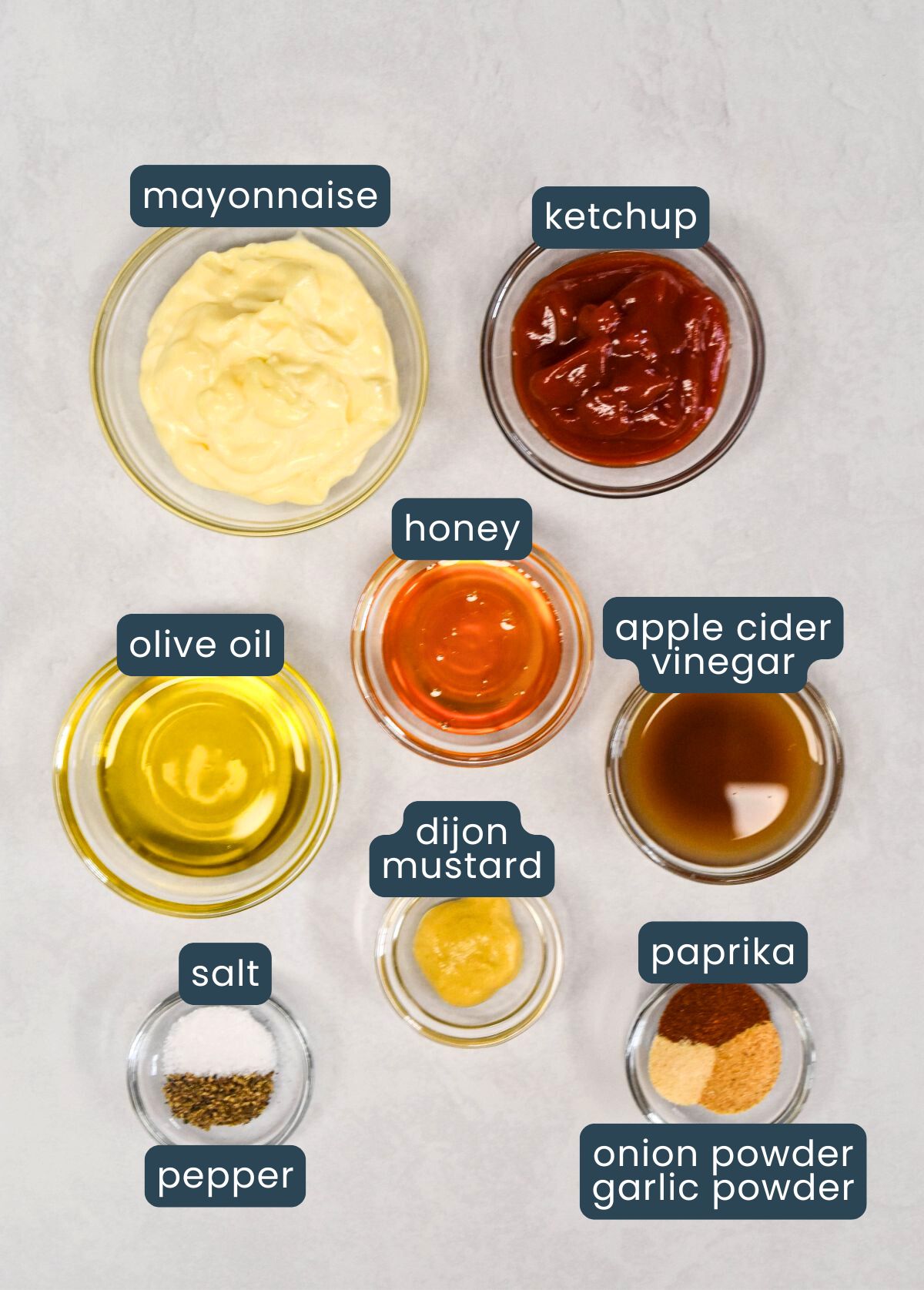 Bowls of ingredients arranged on a light surface, labeled for making homemade dressing.