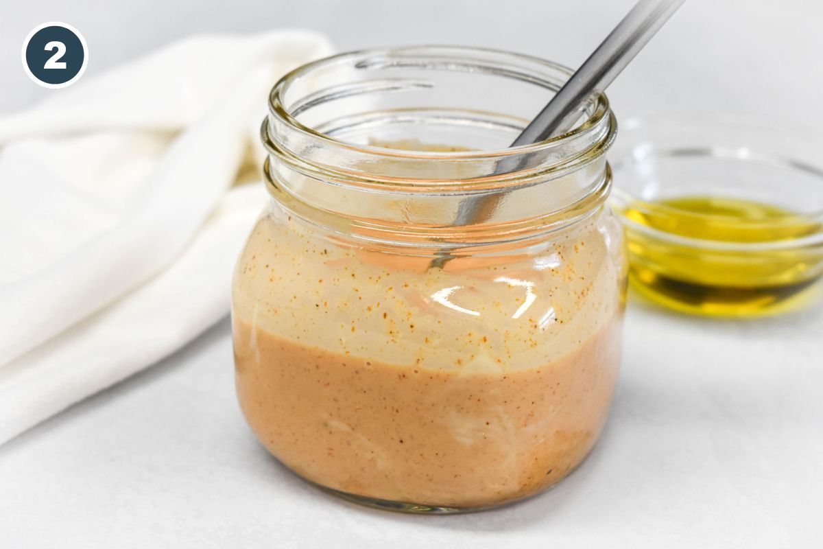 Creamy orange dressing in a jar after mixing, with a spoon inside.