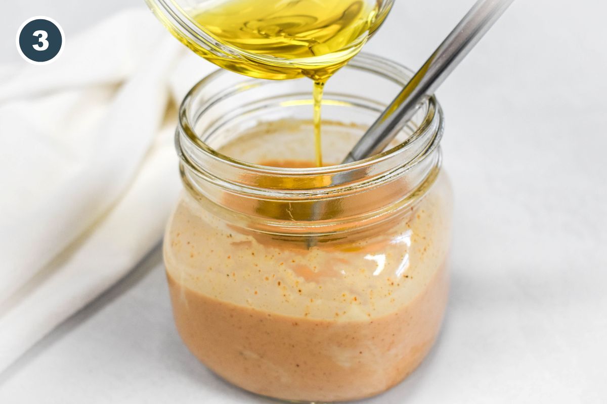 Olive oil being poured into the jar to finish blending the dressing.