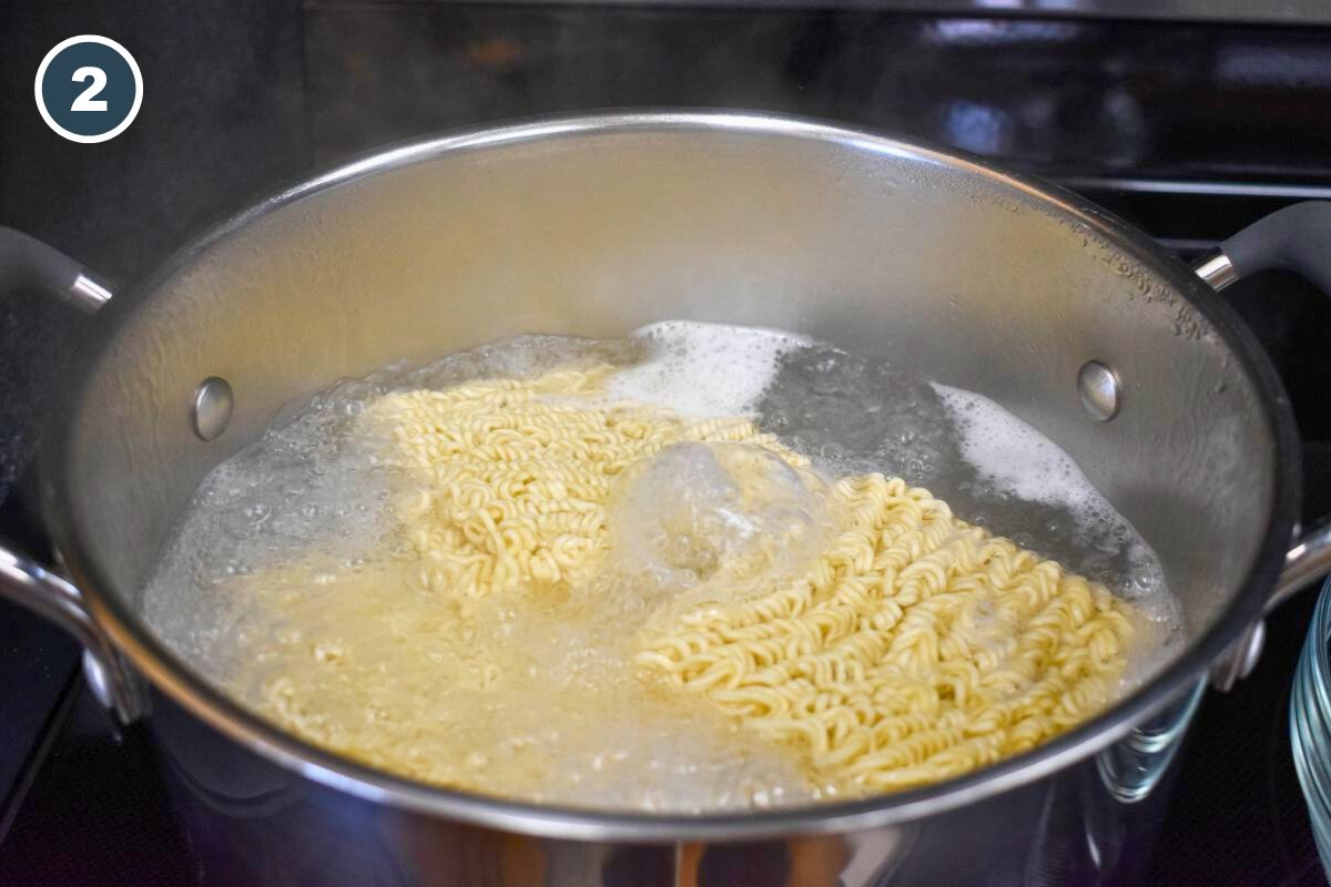 Ramen noodles boiling in a large stainless steel pot of water on the stove.